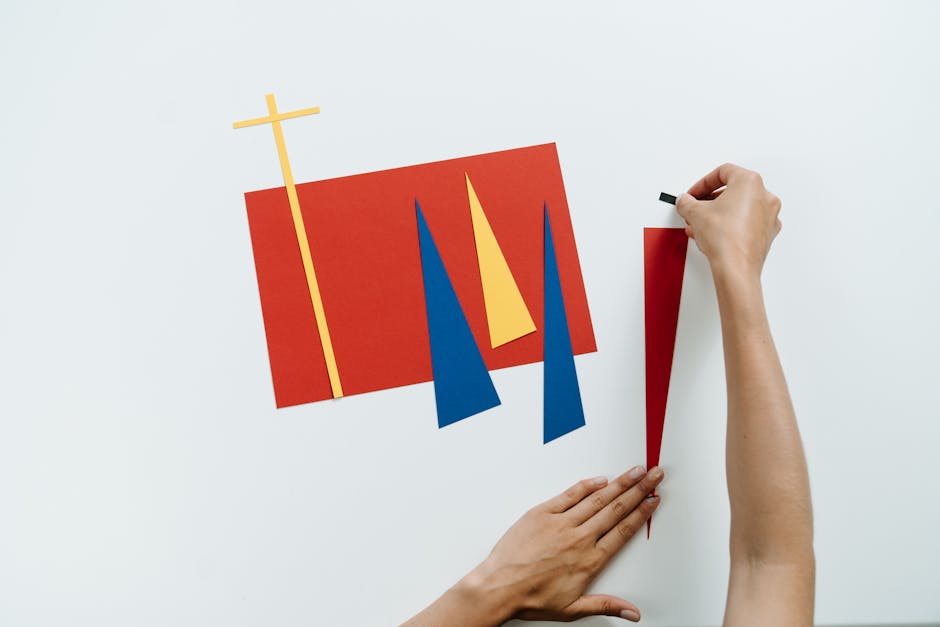 A modern art composition featuring vibrant paper shapes in red, blue, and yellow with hands arranging them creatively.
