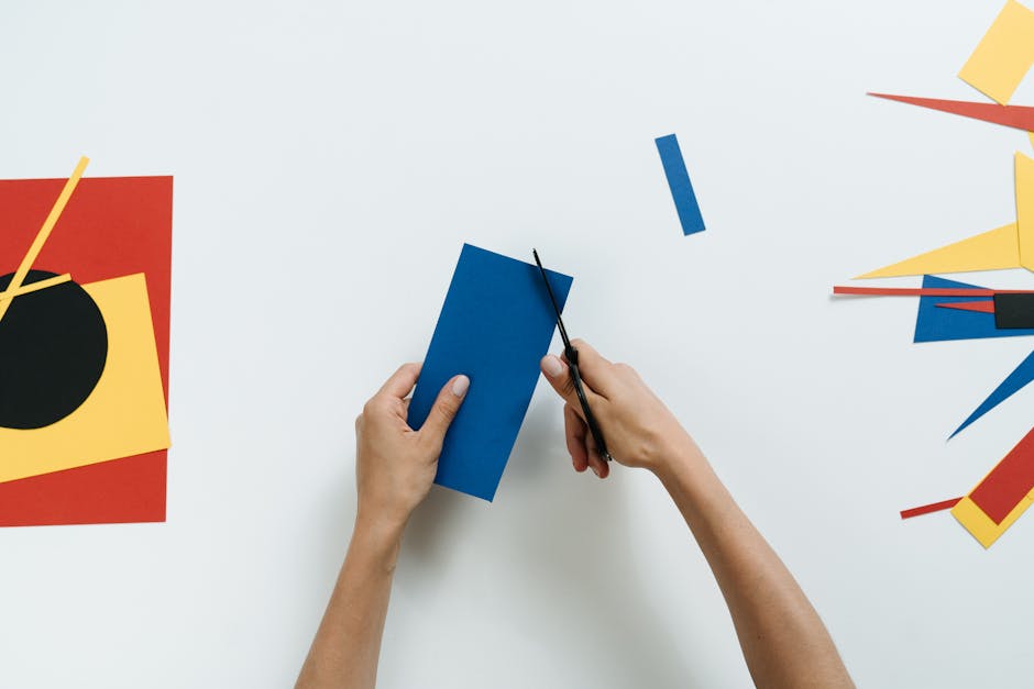 Hands cutting colorful paper for a geometric art project, emphasizing creativity and modernism.